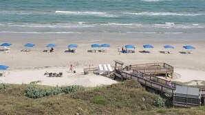 Ein Strand mit blauen Sonnenschirmen und weißen Liegestühlen.