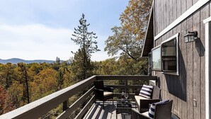 A wooden deck with outdoor furniture and a view of a forested landscape. - Whispering Pines | Amazing Views | Family Fun (Lake Arrowhead)