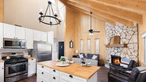 A modern kitchen with white cabinetry, a central island, and a stone fireplace. - Whispering Pines | Amazing Views | Family Fun (Lake Arrowhead)