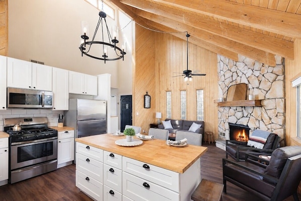 A modern kitchen with white cabinetry, a central island, and a stone fireplace.
