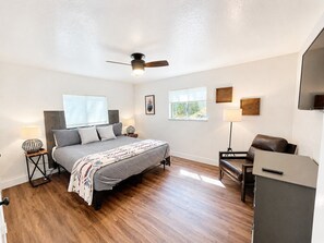 A bedroom with a bed, bedside tables, a desk, a chair, a ceiling fan, and a window. - Whispering Pines | Amazing Views | Family Fun (Lake Arrowhead)