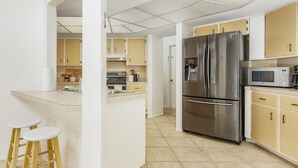 Eine moderne Küche mit einem Edelstahlkühlschrank, einer Mikrowelle und einer kleinen Kochinsel mit Hockern.