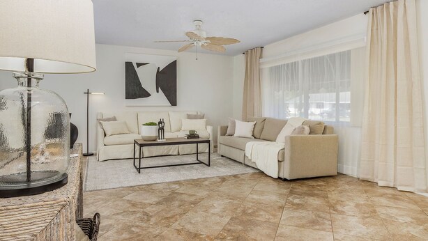 Ein Wohnzimmer mit zwei Sofas, einem Couchtisch, einer Lampe und einem Deckenventilator.