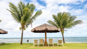 A beachside setting with palm trees, a thatched umbrella, and beach chairs.