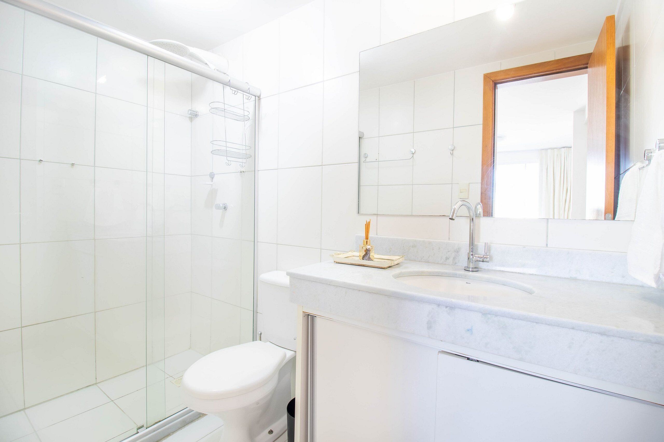 Un baño moderno con cabina de ducha de vidrio, inodoro blanco y lavamanos de mármol con espejo superior.