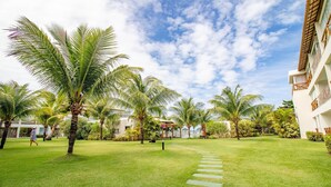 A well-maintained garden with palm trees, a clear sky, and a pathway leading to a building.