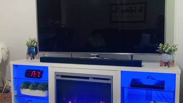 Un televisor de pantalla plana sobre un mueble blanco con chimenea empotrada, estantes y un reloj.