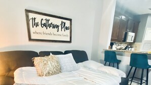 Une chambre à coucher avec un lit, une table basse, une citation encadrée au mur et, au fond, un coin cuisine.