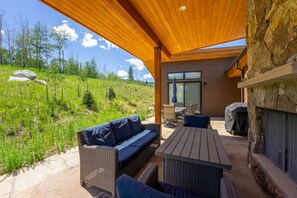 Une terrasse extérieure aménagée avec des meubles en osier, une cheminée en pierre et une vue sur une colline verdoyante.