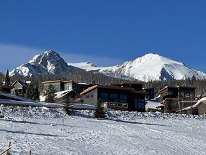 Une montagne enneigée, avec des maisons modernes au premier plan.