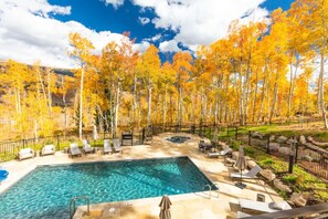 Une piscine dotée de chaises longues et d’un jacuzzi, entourée d’une clôture et d’arbres aux feuilles d’automne.