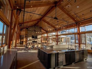 A spacious kitchen with a large island, wooden beams, and large windows offering views of the outdoors. - Mountain Escape | Resort Amenities | Summit Sky Ranch | 3 King Primary Bedroom`s (Silverthorne)