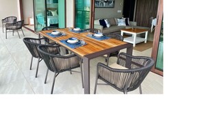 Un coin repas avec une table en bois et des chaises en osier noir, un canapé et une porte-fenêtre coulissante donnant sur un balcon.