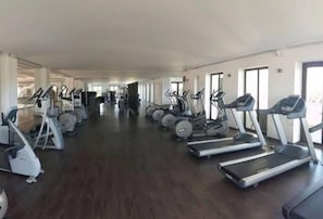Une salle de sport équipée de plusieurs tapis de course et de plusieurs appareils elliptiques disposés en rangées.
