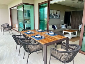 Un coin repas avec une table en bois et des chaises en osier noir, un canapé et une porte-fenêtre coulissante donnant sur un balcon.