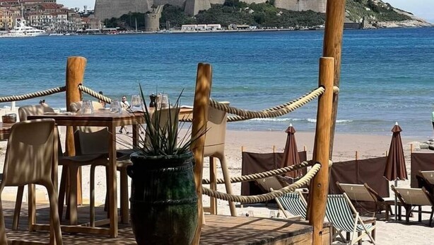 An outdoor dining area with tables and chairs, overlooking a coastal town with historic buildings and a fortification. - Studio Calvi (Corsica) 250 meters from the beach, WiFi (Calvi)