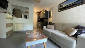 A living room with a sofa, a coffee table, a ceiling fan, a kitchen in the background, and a painting on the wall. - Studio Calvi (Corsica) 250 meters from the beach, WiFi (Calvi)