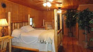 A wooden cabin bedroom with a bed, a nightstand, a lamp, and a ceiling fan. - Guest House with acreage to explore. (Tennyson)