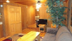 A cozy living room with wooden walls, a sofa, a coffee table, a television, and a potted plant. - Guest House with acreage to explore. (Tennyson)