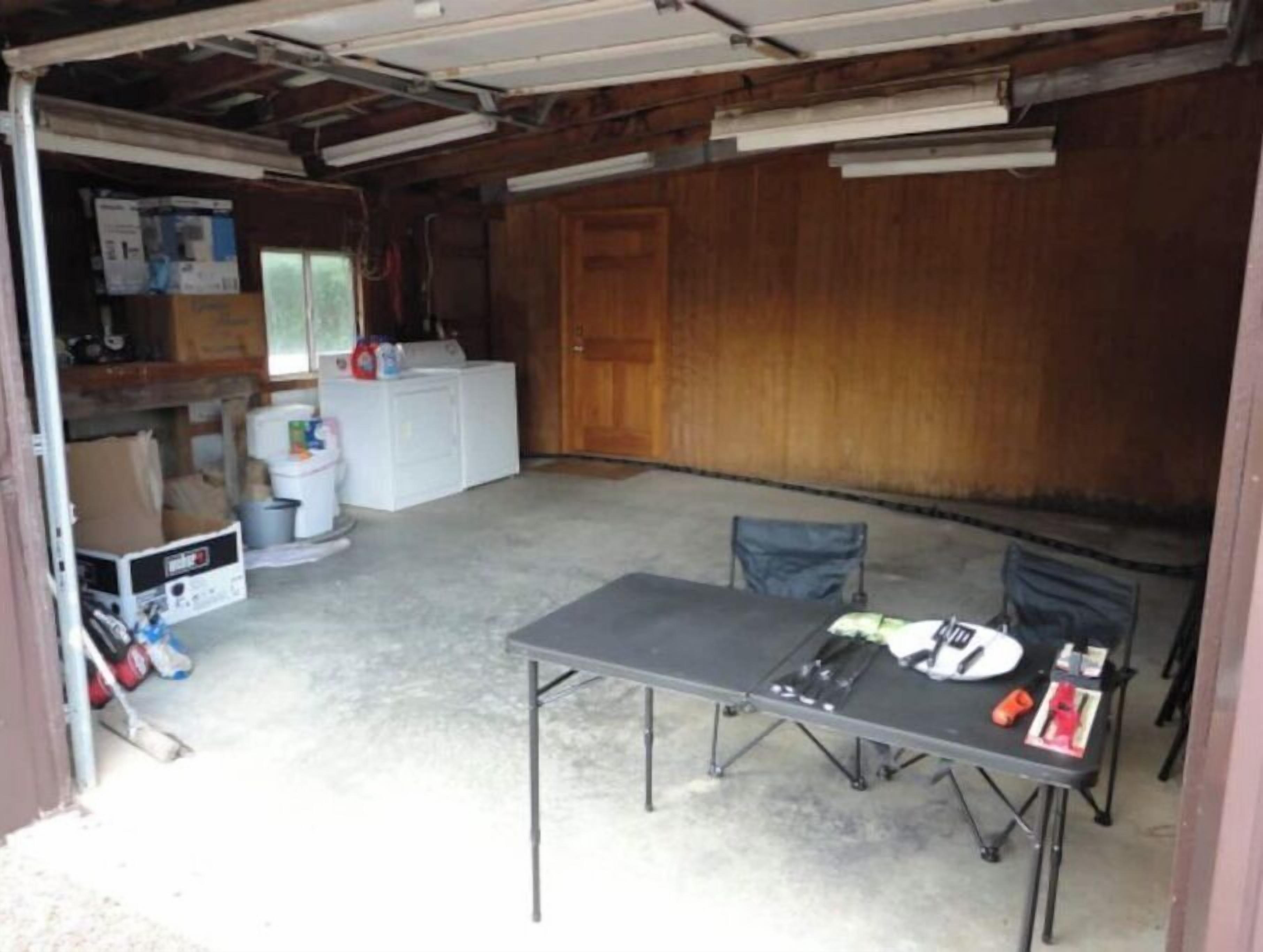Eine Garage mit Tisch, Stühlen, einer Waschmaschine und diversen Gegenständen auf Regalen.