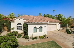 A single-story house with a tiled roof, a garage, and a well-maintained garden with various plants and shrubs.