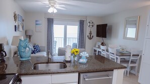A kitchen with a dishwasher, a sink, and a dining area with chairs and a table. - Hot Tub/Pool, Cov’d Parking (Gulf Shores)