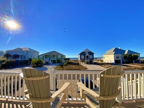 A beachfront property with a wooden deck, beach chairs, and houses with varying roof colors.