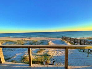A beach view from a wooden deck with a wooden railing.