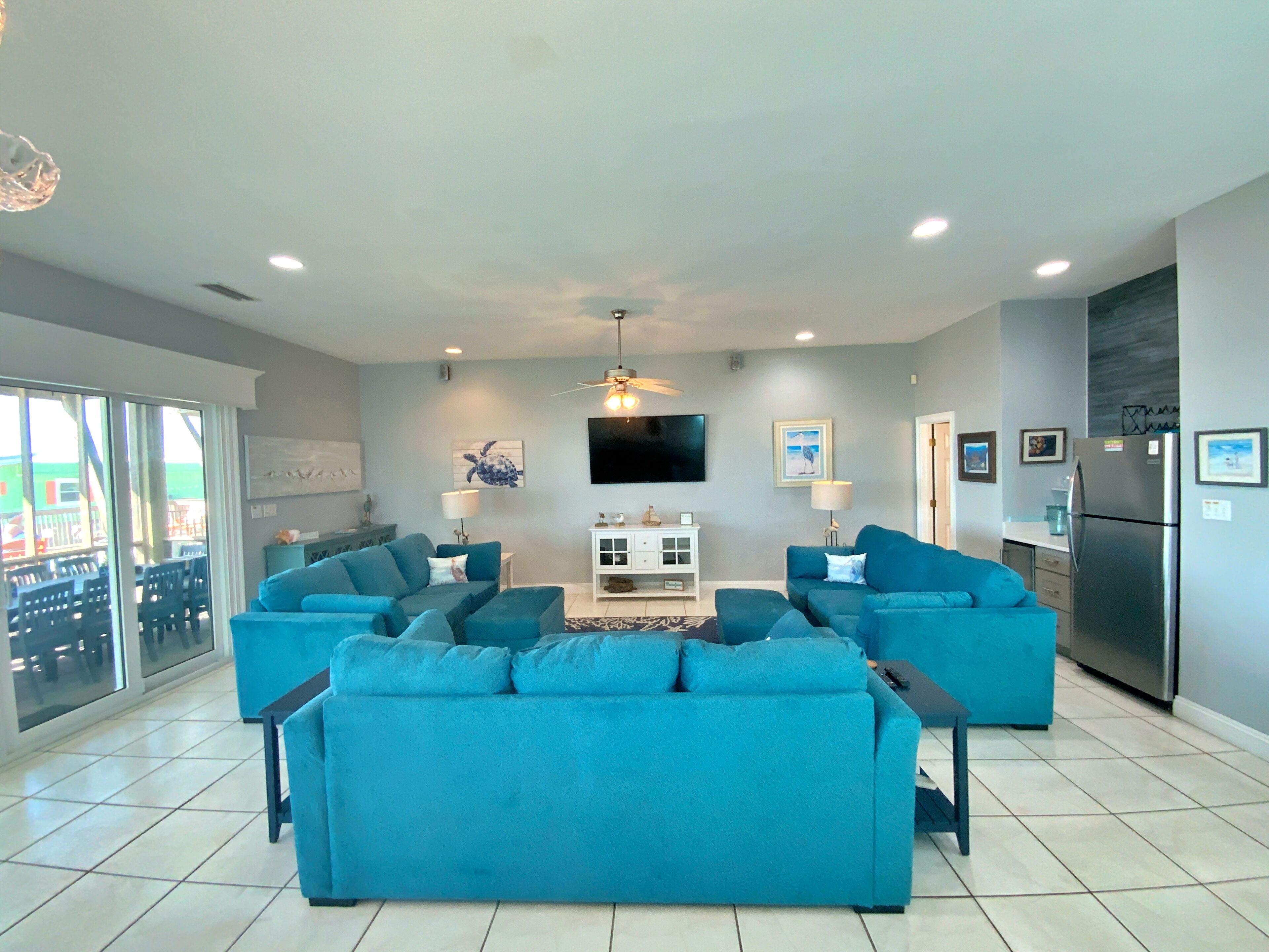 A modern living room with two large blue sofas, a flat-screen TV, and a ceiling fan.