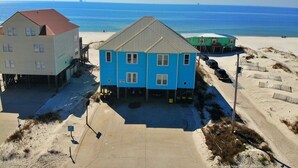 Ein Küstenhaus mit blauer Fassade, grauem Dach und einem Sandstrand im Hintergrund.