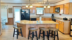 Una cocina con armarios de madera, una isla central con taburetes, un refrigerador y un microondas.