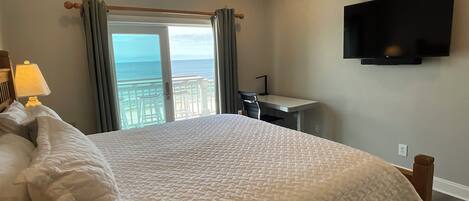 Une chambre d’hôtel équipée d’un lit, d’un bureau, d’une télévision et d’un balcon avec vue sur l’océan.