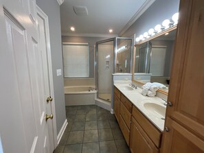 Un baño moderno con cabina de ducha a ras de suelo, bañera y tocador con un espejo grande e iluminación.