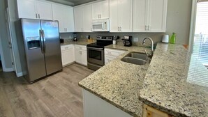 A modern kitchen with white cabinets, stainless steel appliances, granite countertops, and a built-in oven. - Beachfront w/ Pool! Sleeps 20 (Gulf Shores)