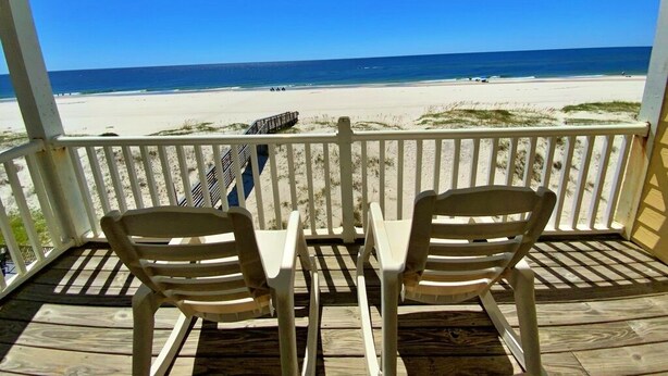 A wooden deck with two chairs and a table overlooking a beach. - Beachfront w/ Pool! Sleeps 20 (Gulf Shores)