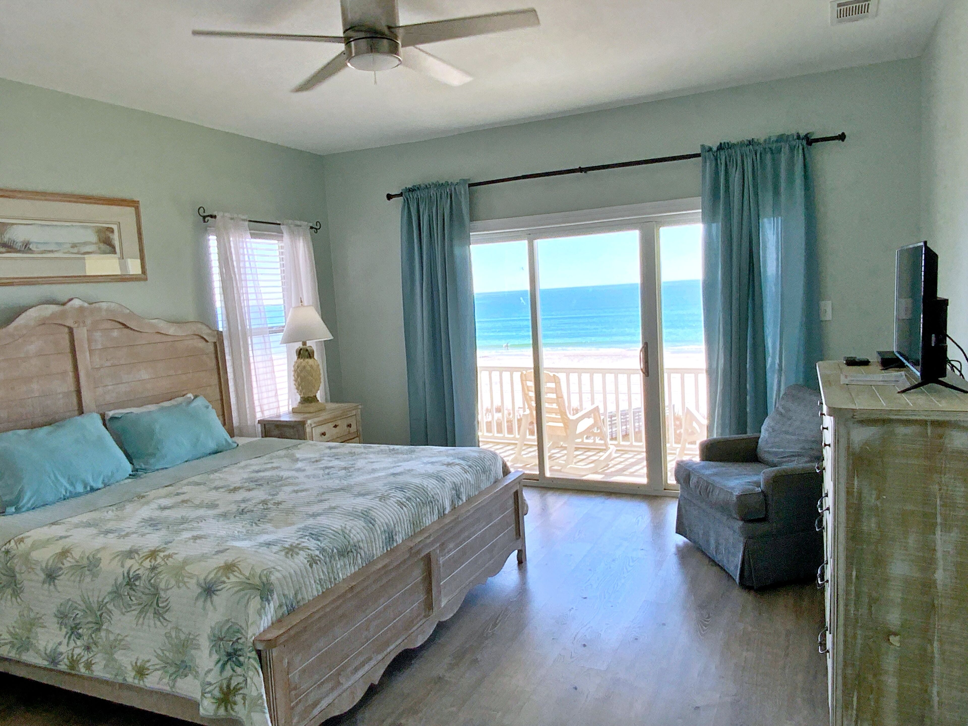 A bedroom with a bed, a desk, a chair, and a view of the beach.