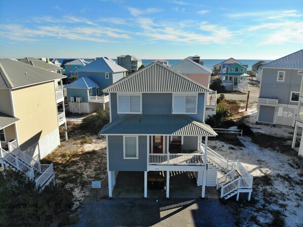 A beachfront property with a two-story house featuring a balcony, a covered porch, and a staircase leading to the entrance. - Pools & Tennis, Pickleball! (Gulf Shores)
