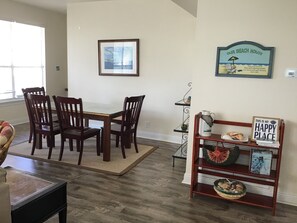 A dining area with a wooden table and chairs, a framed picture on the wall, and a shelf with a 'Happy Place' sign. - Pools & Tennis, Pickleball! (Gulf Shores)
