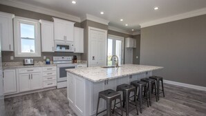A modern kitchen with white cabinetry, a granite countertop, and a central island with bar stools. - Shared Private Beach Walk, Pools & Pickleball (Gulf Shores)