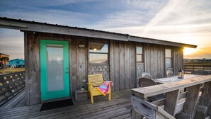 Uma cabana de madeira com uma porta azul-turquesa, um banco e uma mesa com cadeiras.
