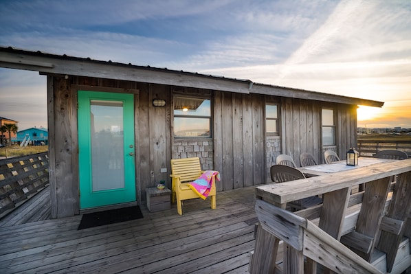 A wooden cabin with a turquoise door, a bench, and a table with chairs.