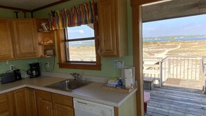 Cozinha com armários de madeira, lava-louças, cafeteira e janela com vista para a praia.