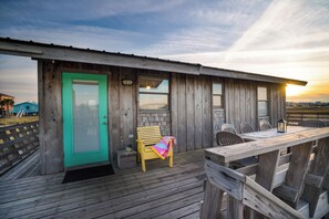 Una cabaña de madera con una puerta turquesa, un banco y una mesa con sillas.