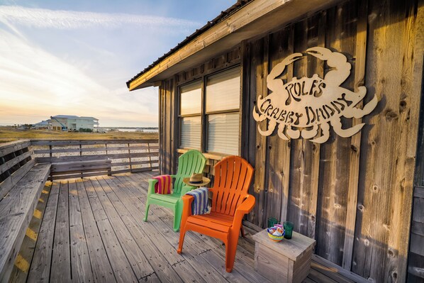 Una terraza de madera con dos sillas Adirondack, una mesita y un letrero que dice "RULF'S CRAB & DUMNY".