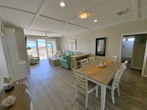 A spacious living area with a dining table, white chairs, a sofa, and a ceiling fan.