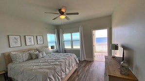 Un dormitorio con cama, ventilador de techo, escritorio de madera y vista al océano.
