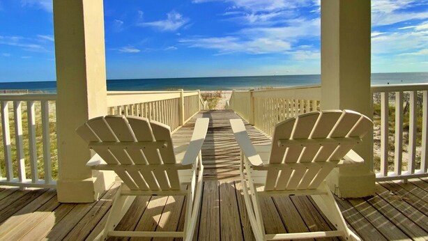 Una terraza de madera con dos sillas Adirondack mirando a la playa.