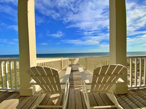 Una terraza de madera con dos sillas Adirondack mirando a la playa.