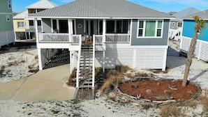 A beachfront house with a covered porch, a small deck, and a sandy surrounding. - Easy Beach Access & Pools!  Morgantown (Gulf Shores)
