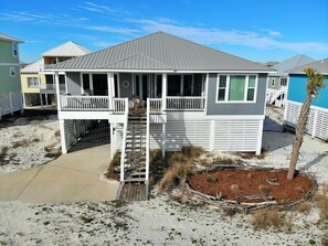 A beachfront house with a covered porch, a small deck, and a sandy surrounding.